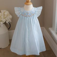 This Baby Girl's Blue Smocked Dress Is Too Cute!! The Dress Is Done In A Pale Blue Voile Atop A White Liner (Poly/Cotton Blend For Easy Care). The Semi-Sheer Voile Adds A Wispy, Dressy Look (True To Many Of Luli & Me's Designs) The Smocked Neckline Has Gorgeous Hand-Embroidered Flowers Done In Shades Of Pink With Light Green, Blue And Yellow Accents, All Atop An Embroidered Lattice Design. The Shoulders Have A Double Ruffle Flutter Sleeve, Which Add Even More Sweetness To The Dress. A Matching B Cotton Smocked Dress With Ruffles For Baptism, Blue Smocked Dress With Flutter Sleeves And Ruffles, Blue Smocked Dress With Cuffs For Playtime, Blue Smocked Dress With Smocked Cuffs For Playtime, Blue Embroidered Cotton Smocked Dress, Cute Blue Smocked Dress With Ruffles, Blue Dress With Smocked Bodice For Playtime, Cute Blue Dresses With Smocked Cuffs, Cute Blue Dress With Smocked Cuffs