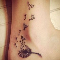 a dandelion tattoo on the ankle with birds flying around it and leaves blowing in the wind