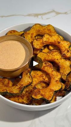 a white bowl filled with cooked zucchini chips and a dipping sauce on top