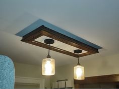 two mason jar lights hanging from a wooden beam in a kitchen with the light turned on