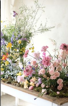 an arrangement of flowers on a table in front of a white wall and window sill