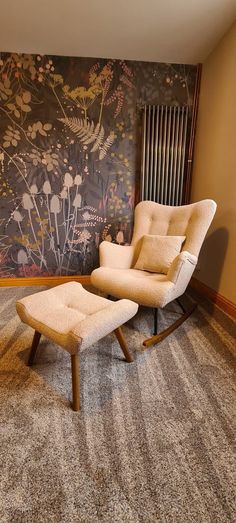 a chair and ottoman in front of a wall with flowers painted on the wall behind it