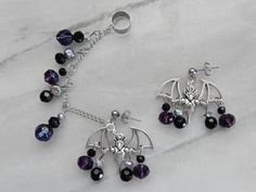 "🦇 Be extra glamorous and show your love for bats when you wear your purple and black bat chained ear cuffs! Purple and black beads accent the silver plated bat charms in these lightweight earrings. 🦇 Drops approximately 1.25\" from the ear posts 🦇 Hypoallergenic, nickel-free ear posts and cuff 🦇 Comes ready-to-gift in a black, cotton-filled box and black satin bag 🦇 We understand accidents happen. If something happens to your earrings to damage them, please contact me for a free repair. Al Purple And Black Jewelry, Emo Pierced Jewelry For Halloween, Purple Earrings For Halloween Party, Silver Gothic Ear Cuff For Party, Purple Metal Jewelry For Halloween, Gothic Purple Jewelry For Halloween, Edgy Purple Jewelry For Gifts, Edgy Purple Jewelry For Gift, Edgy Purple Jewelry As Gift