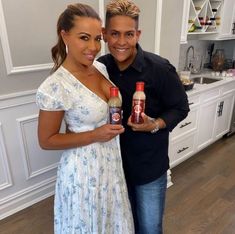 a man and woman standing next to each other holding two bottles of ketchup