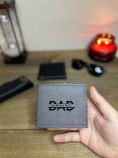 a person holding up a leather wallet with the word dad on it in front of some other items