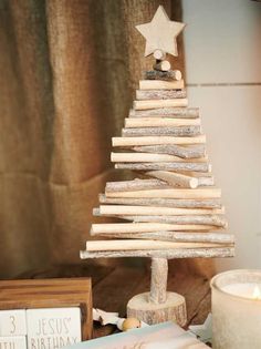 a small wooden christmas tree sitting on top of a table next to a candle and books