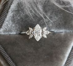 a diamond ring sitting on top of a gray velvet bag with feathers flying around it