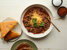 a bowl of chili next to two slices of bread and some other food on plates