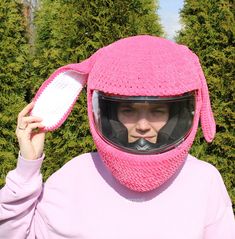 a woman wearing a pink knitted helmet and holding a comb in front of her face