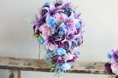 a bridal bouquet with purple and blue flowers on a wooden bench in front of a white wall