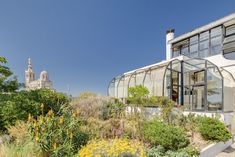 a building with lots of plants and flowers in front of it on a sunny day