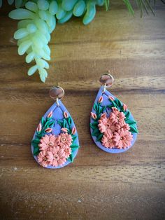 two earrings with flowers on them sitting next to a plant