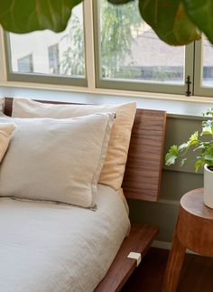 a bed with two pillows on top of it next to a plant in a vase