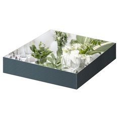 a glass tray with flowers and greenery on the bottom, in front of a white background