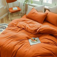 an orange comforter on a bed in a room with two chairs and a potted plant