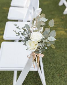 white chairs with flowers and greenery tied to them on the grass at an outdoor ceremony