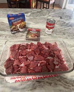 raw meat in a glass baking dish on a kitchen counter next to two cans of ice cream