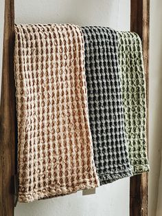 three different colored towels hanging on a wooden rack next to a white wall and window