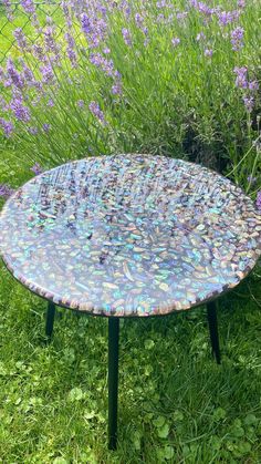 a table that is sitting in the grass near some purple flowers and lavenders with lots of stones on it