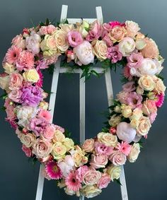 a heart shaped wreath with pink and white flowers on an easel against a gray background