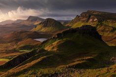 the mountains are covered with green grass and clouds in the distance is a body of water