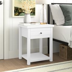 a white night stand with a lamp on it next to a bed in a bedroom