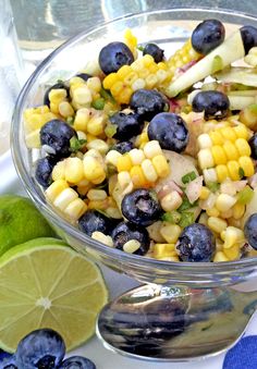 a glass bowl filled with corn and blueberries next to lime wedges on a table