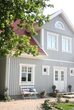 a large gray house with white trim on the front and side windows, along with two lawn chairs