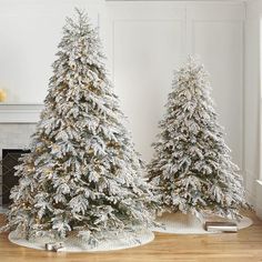 two white christmas trees in front of a fireplace with snow on the top and bottom