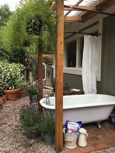 a bath tub sitting under a pergolated roof next to a flower bed and potted plants