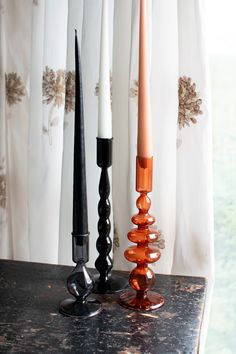 an assortment of candles sitting on top of a black table next to white drapes