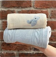 a person holding two blankets in front of a brick wall with an elephant on them