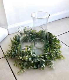 two vases sitting on top of a tile floor next to a wreath with greenery