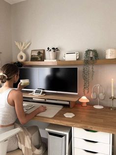 a woman sitting at a desk in front of a computer on top of a wooden desk