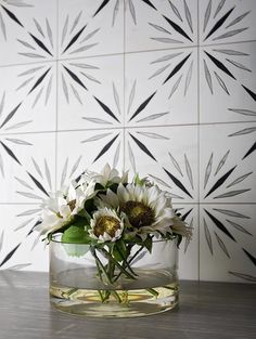 a vase filled with white flowers on top of a wooden table next to a tiled wall