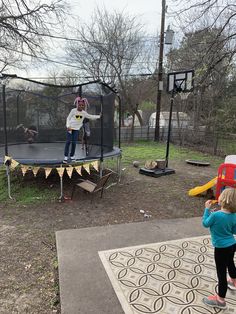 two children are playing on a trampoline in the yard