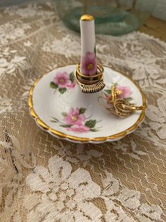 a white and gold plate with pink flowers on it sitting on a lace tablecloth