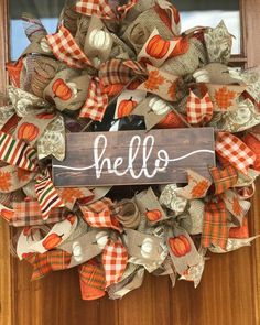 a wreath with the word hello written on it and pumpkins hanging from the front door