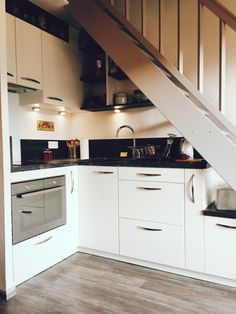 a kitchen with white cupboards and black counter tops under a stair case in an apartment