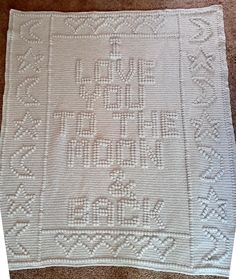 a white crocheted afghan with the words love written on it, sitting on a carpet