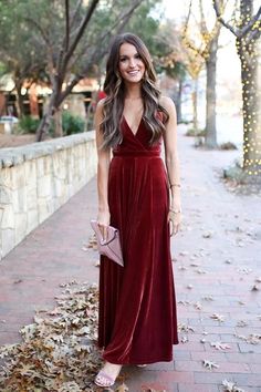 a woman in a long red dress standing on the sidewalk with leaves all around her