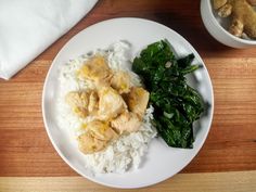 a white plate topped with rice and chicken next to spinach on a wooden table