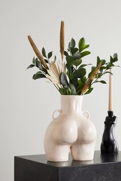 two white vases with plants in them on a black table next to each other