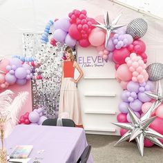 a woman standing in front of a balloon arch with stars and balloons on the wall