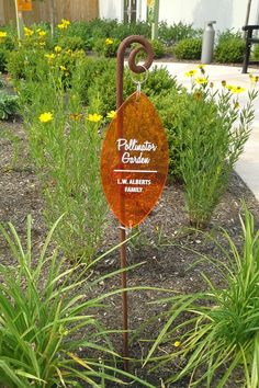 a sign that is in the grass near some flowers and plants with yellow flowers behind it