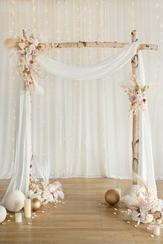 a white wedding arch decorated with flowers and gold balls on the floor next to candles