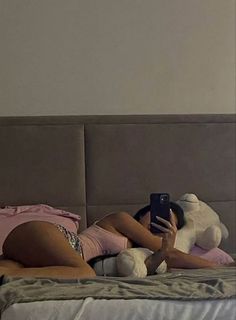 a woman laying in bed with her cell phone up to her chest and holding a teddy bear