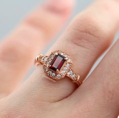 Gorgeous Vintage Inspired Garnet Ring ►Made of solid sterling silver with the 14k rose gold finish (925) ►Accented With Simulated Diamonds (CZ) ►Average band width: 2.3 mm ►Halo size: 9.9mm x 8.3mm Center Stone: Garnet Stone Cut: Emerald Measurements: 4.0 x 6.0 mm Carat Weight: 0.7 ct. (approx.) Gemstone creation: 100% Natural Hardness: 7.5 (Mohs scale) ►Average band width: 1.6 mm ►Please be aware that plated jewelry can wear off over time, if this is a concern we would suggest going with the st Classic 14k Rose Gold Ruby Ring For Anniversary, Classic Rose Gold Ruby Promise Ring, Classic Rose Gold Ruby Ring For Proposal, Classic Rose Gold Ruby Ring With Halo Setting, Antique Promise Rings, Garnet Engagement Ring, Natural Opal Ring, Popular Engagement Rings, Red Gemstones