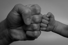 a black and white photo of two hands holding each other's fist, with one hand reaching out towards the other