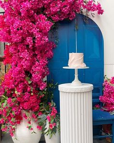 a cake sitting on top of a white pedestal next to flowers and a blue door